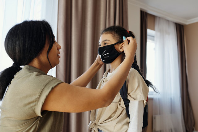 A mother puts a face mask on her daughter as they head to a lice clinic